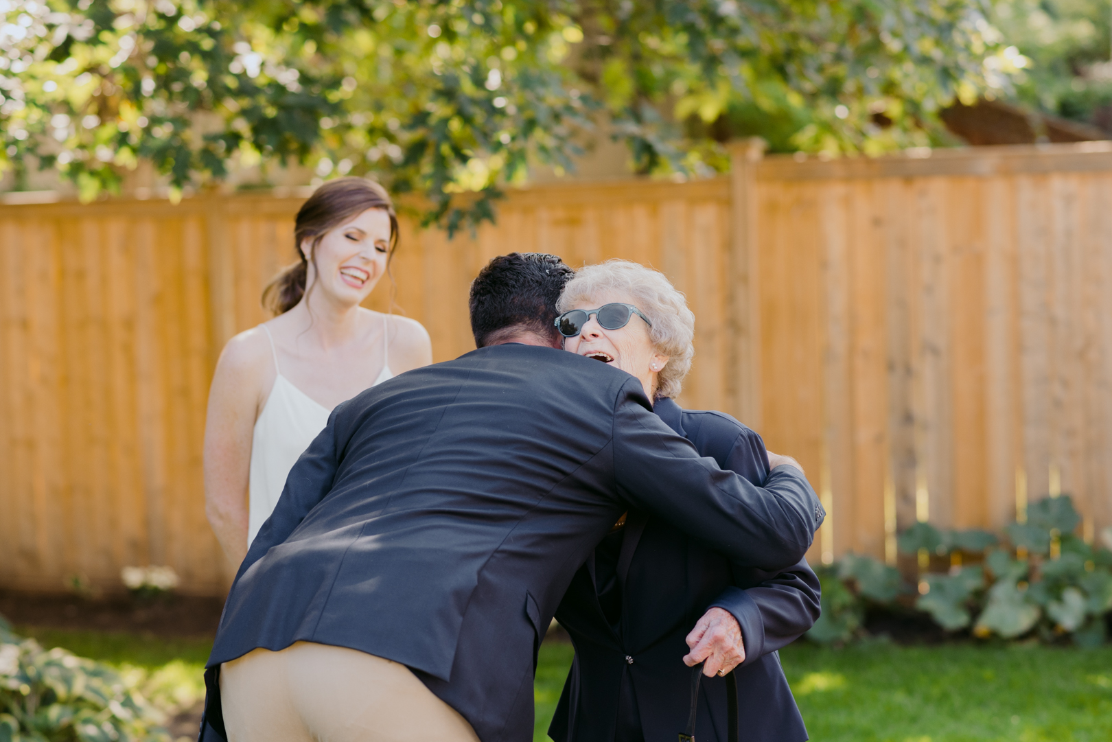 groom hugging his grandmother as she arrives to backyard wedding ceremony