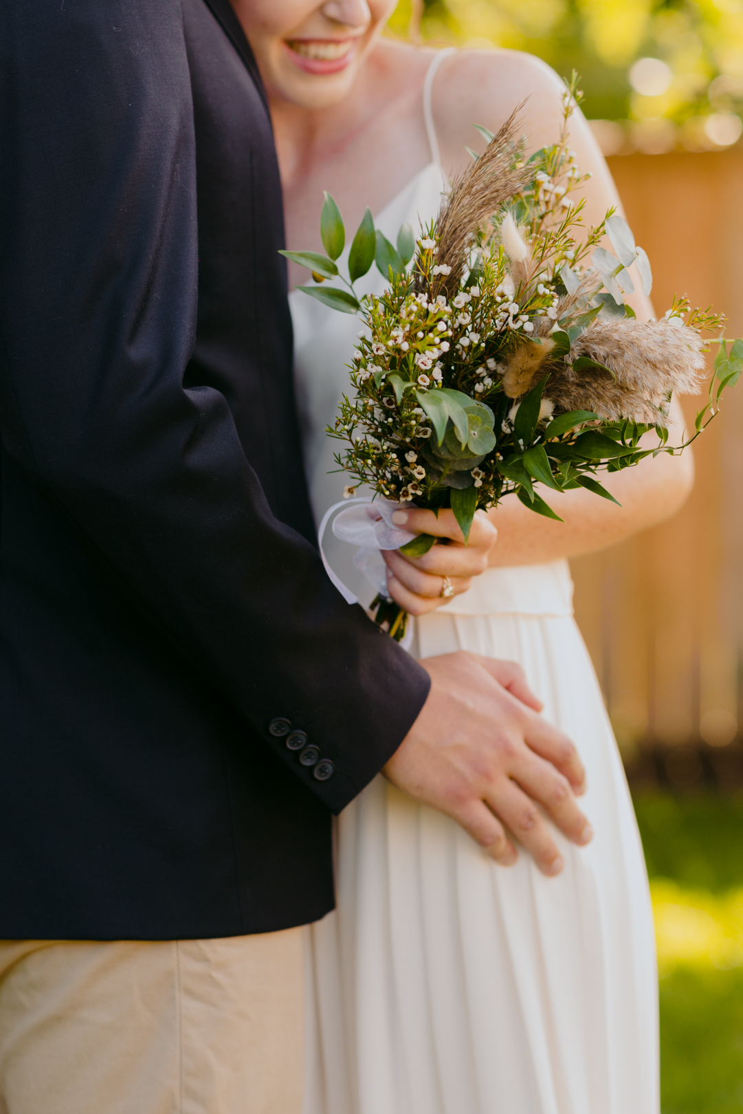 bride holding wild bouquet while resting her head on groom's chest