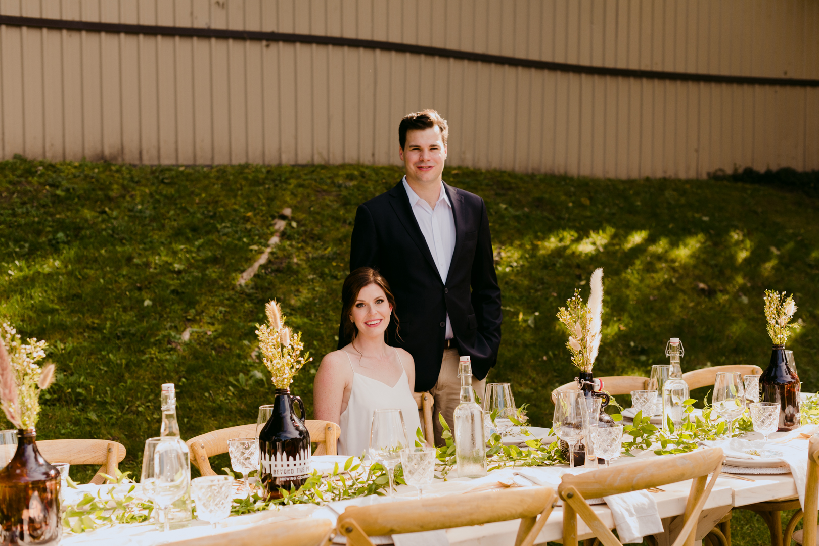 bride and groom sitting at harvest table at backyard wedding