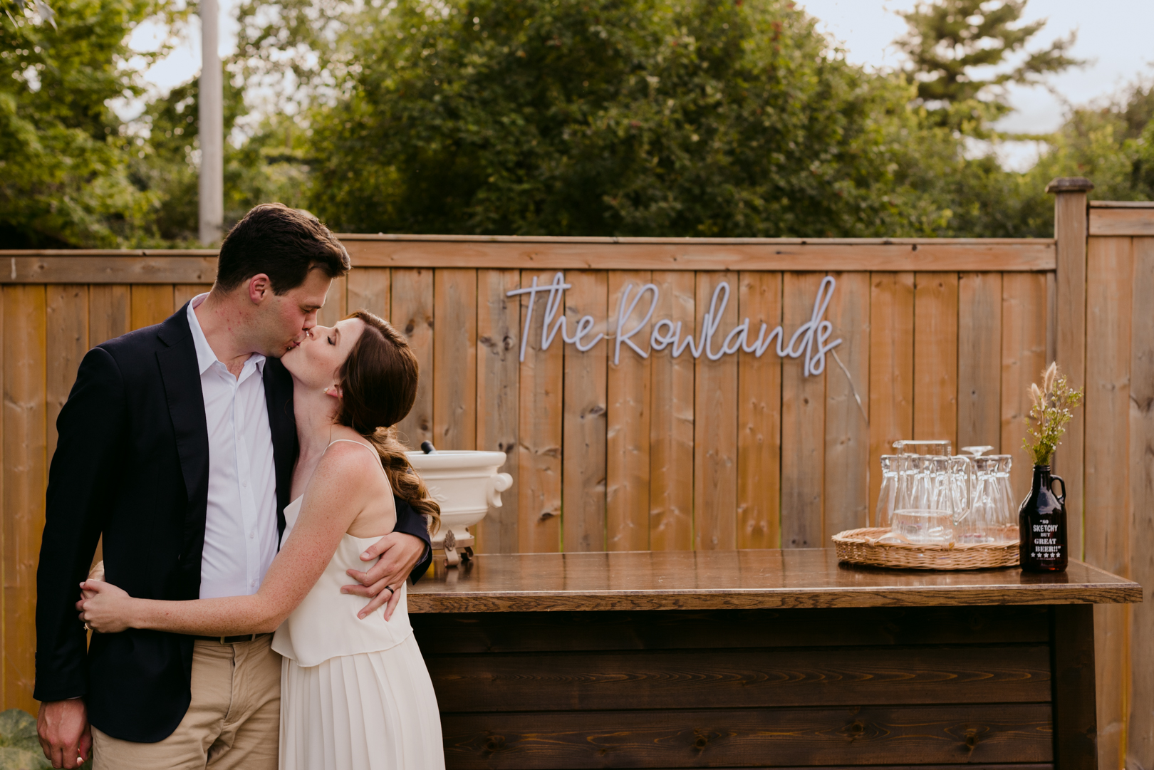 bride and groom kissing in front of wooden bar with neon sign with their names