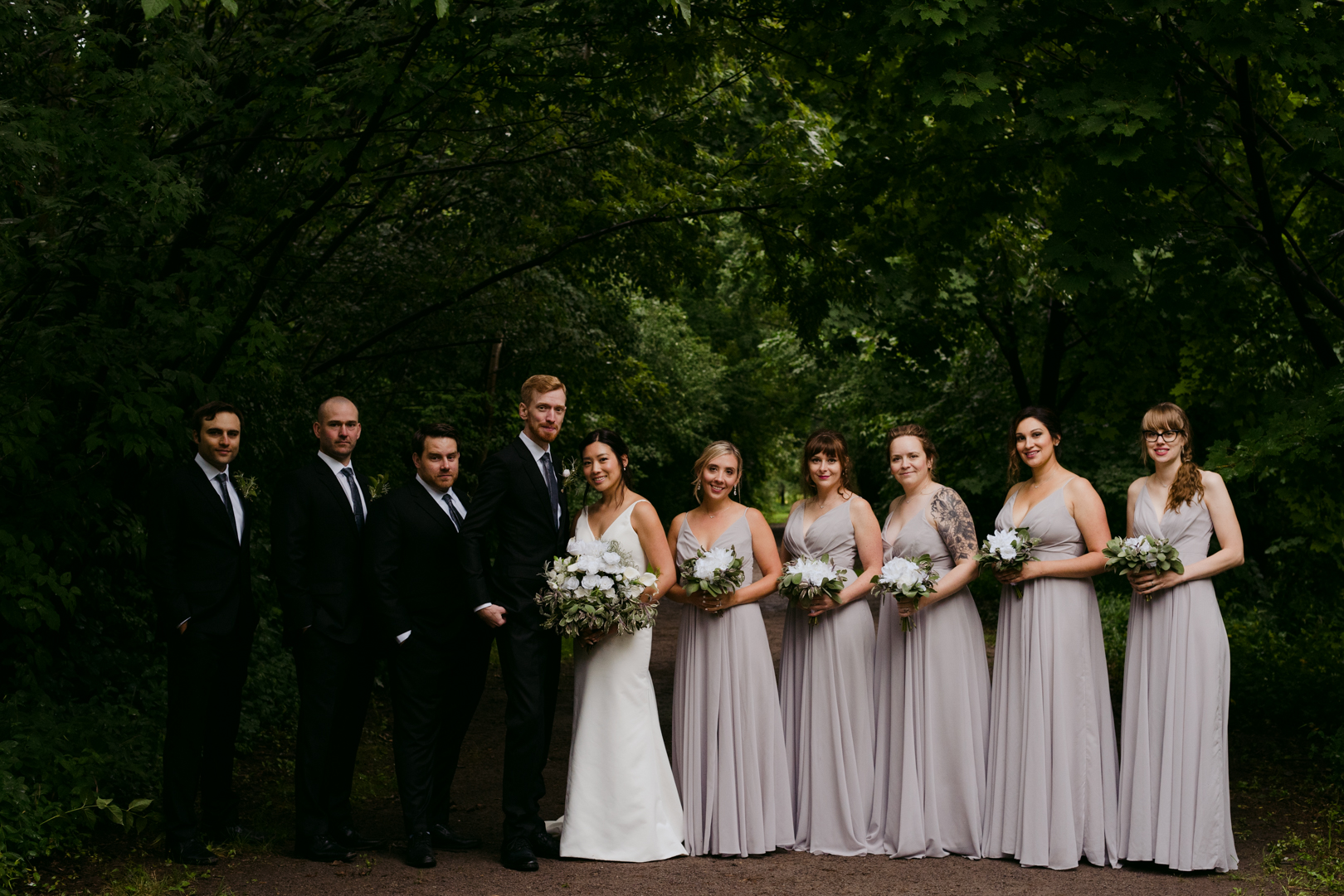 wedding party standing under the trees in a forest smiling at the camera