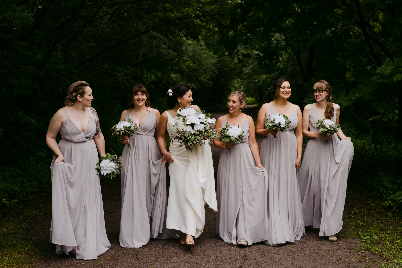bride and bridesmaids walking down path in the woods