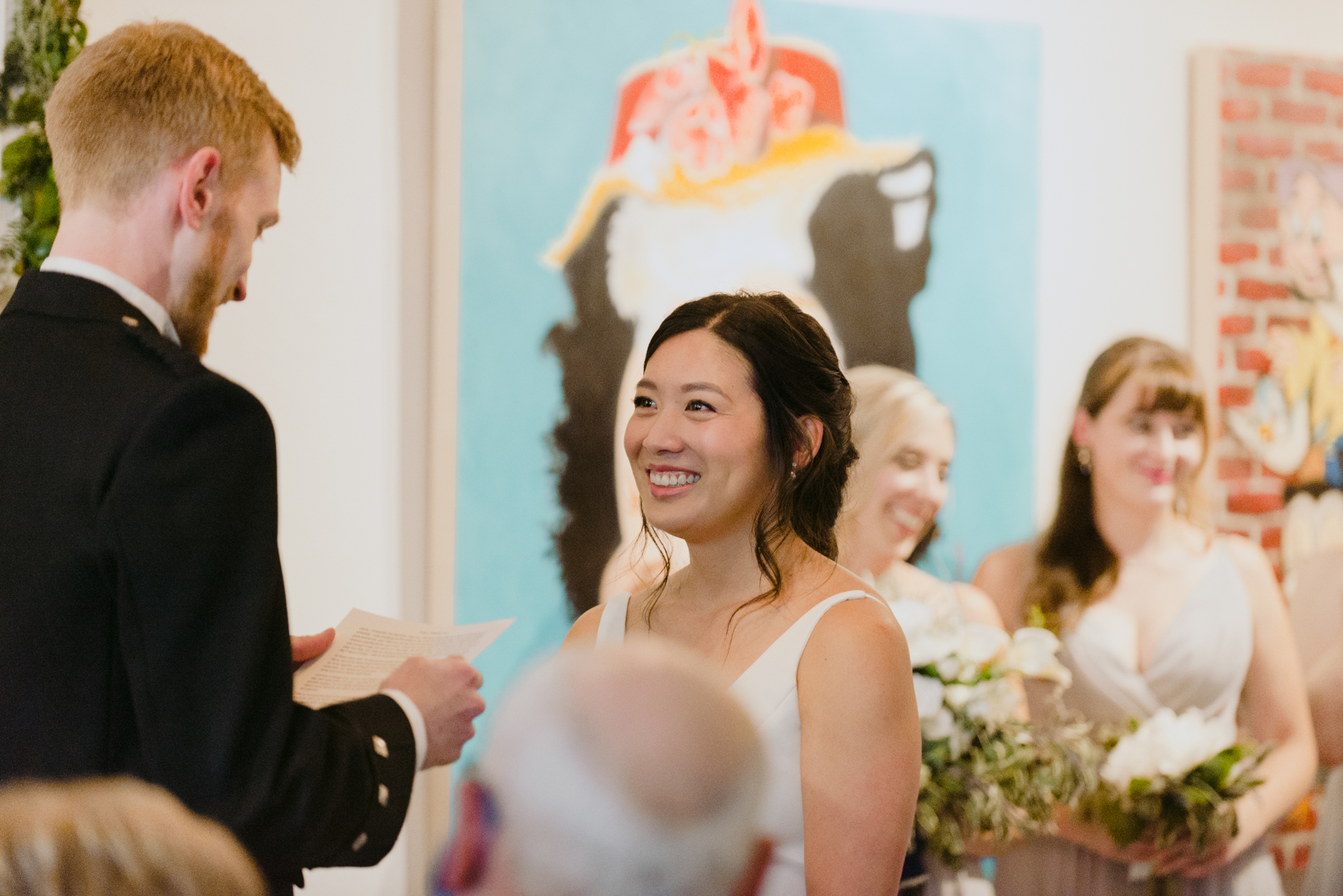 bride smiling at groom while he reads his vows at Orange Art Gallery wedding