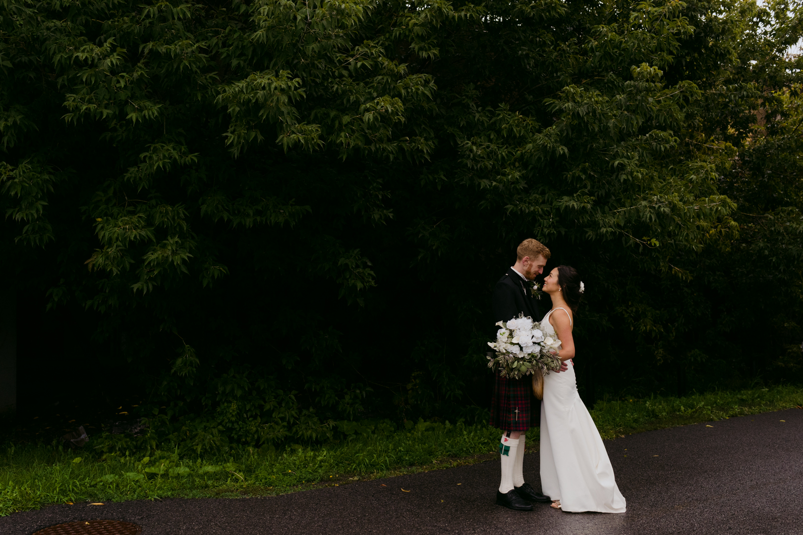 bride standing with groom wearing a kilt in the trees