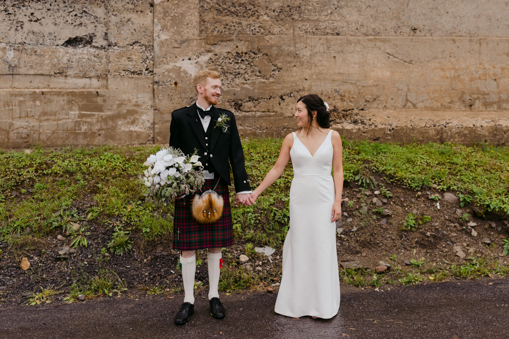 groom holding bouquet wearing a kilt holding his bride's hand