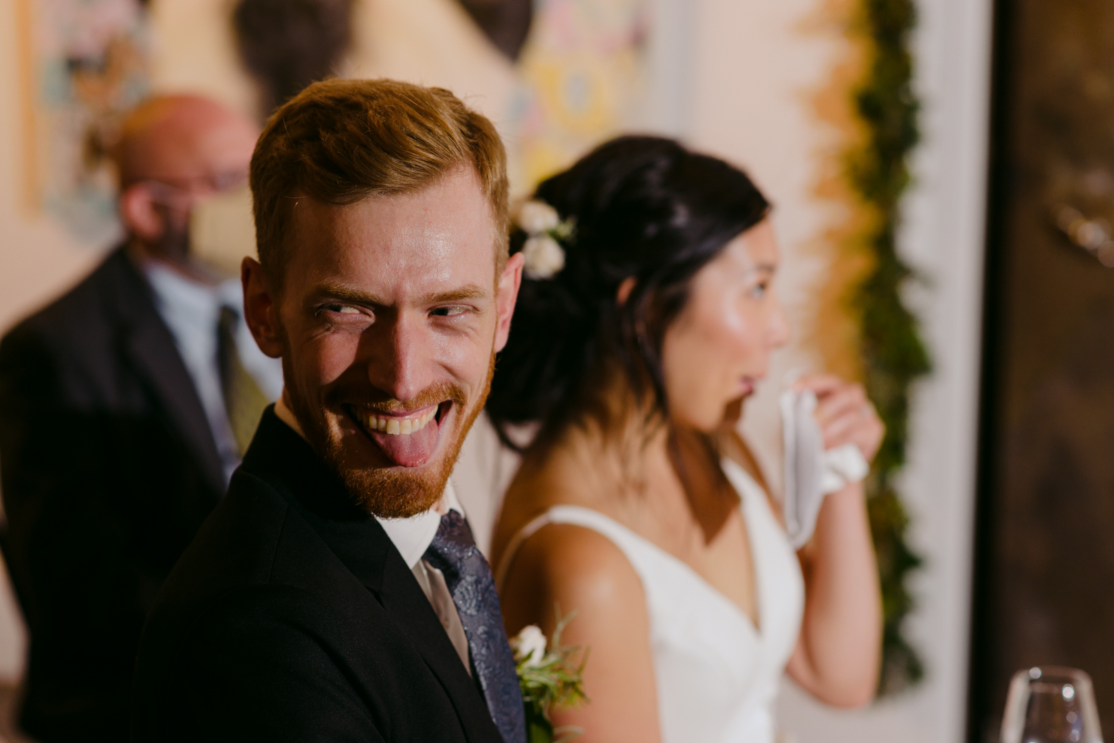 groom laughing and sticking out his tongue during speeches at Orange Art Gallery wedding
