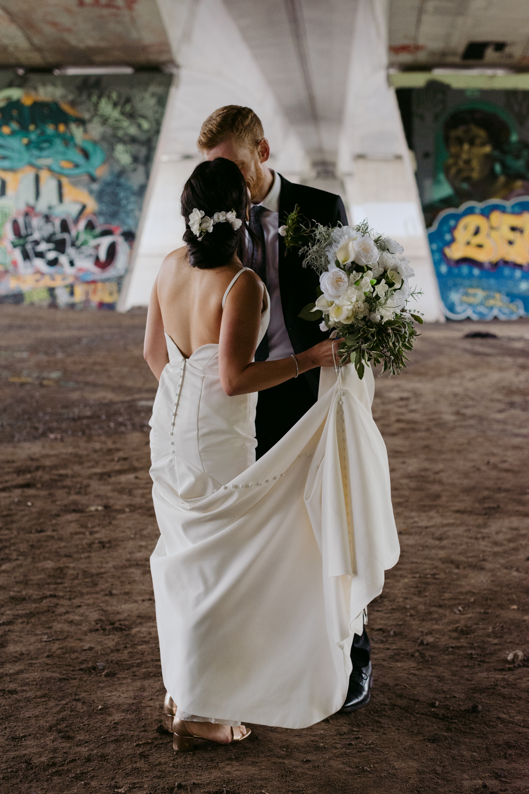 bride and groom kissing after first look underneath a bridge with graffiti