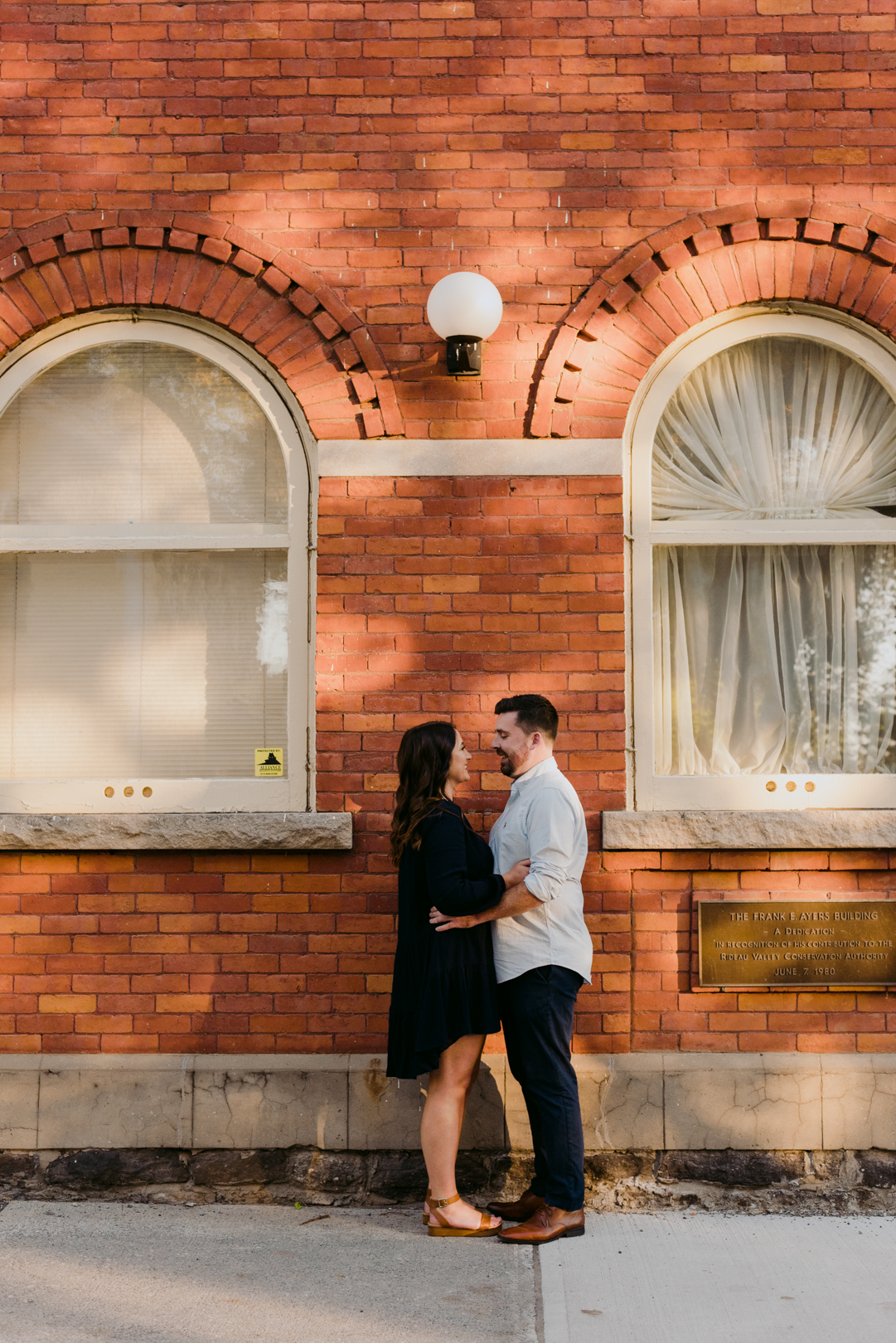 engaged couple cuddling in front of old red brick building and window panes