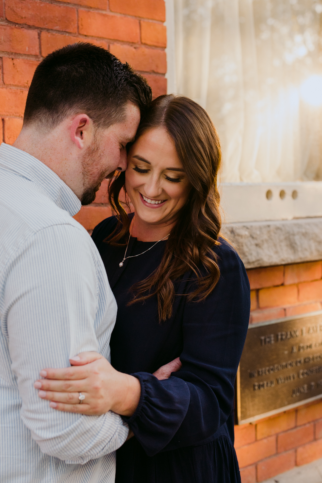 engaged couple cuddling at sunset by red brick building