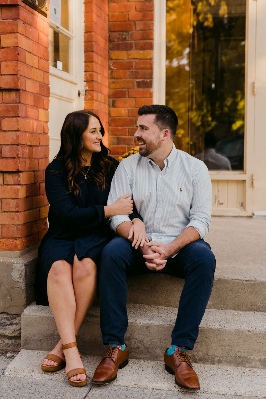 engaged couple sitting on steps of old red brick building at sunset