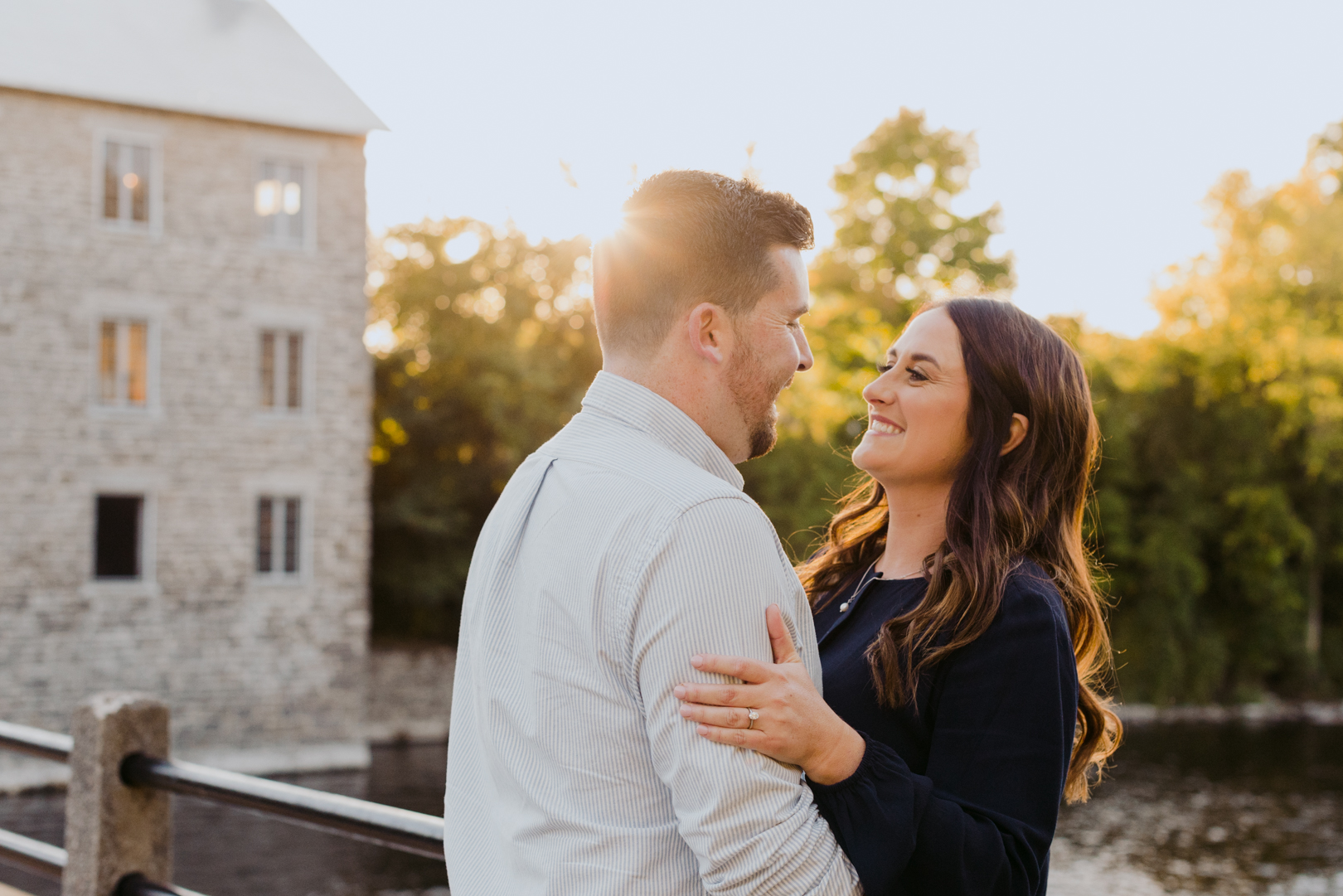 engaged couple cuddling by Watson's Mill at sunset