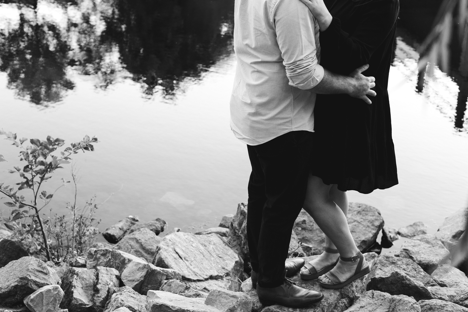 engaged couple's legs standing on rocks by the water in black and white