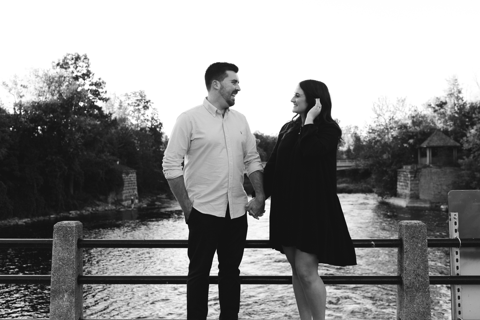 Engaged couple standing on a bridge holding hands in black and white