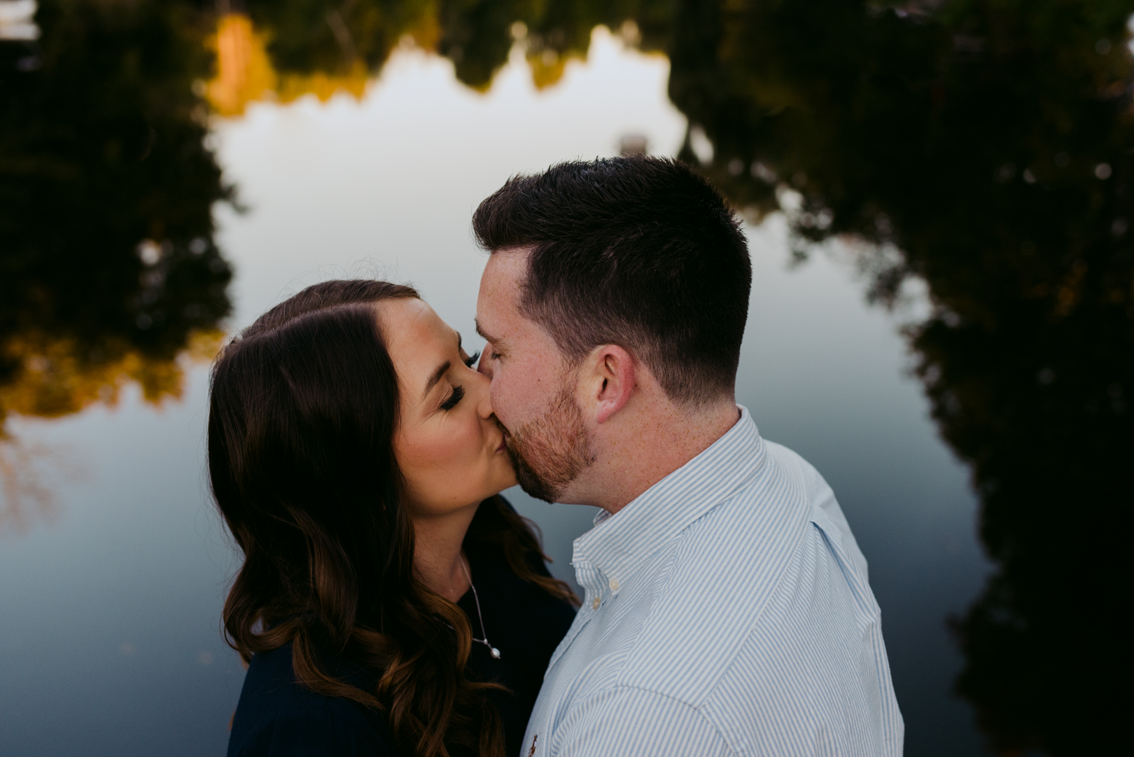 engaged couple kissing with the water reflected in the background