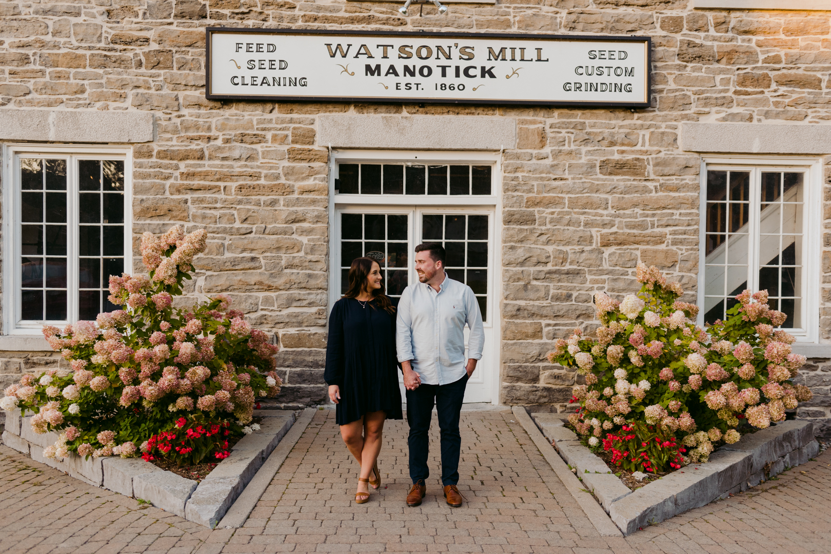 engaged couple holding hands in front of Watson's Mill in Manotick