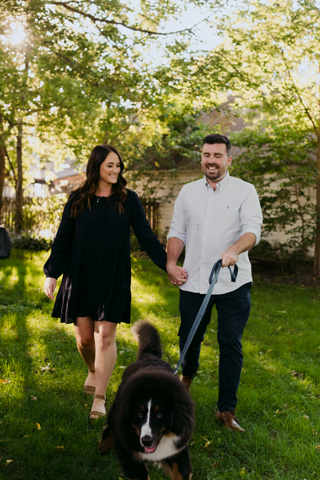 engaged couple holding hands walking their dog through the grass
