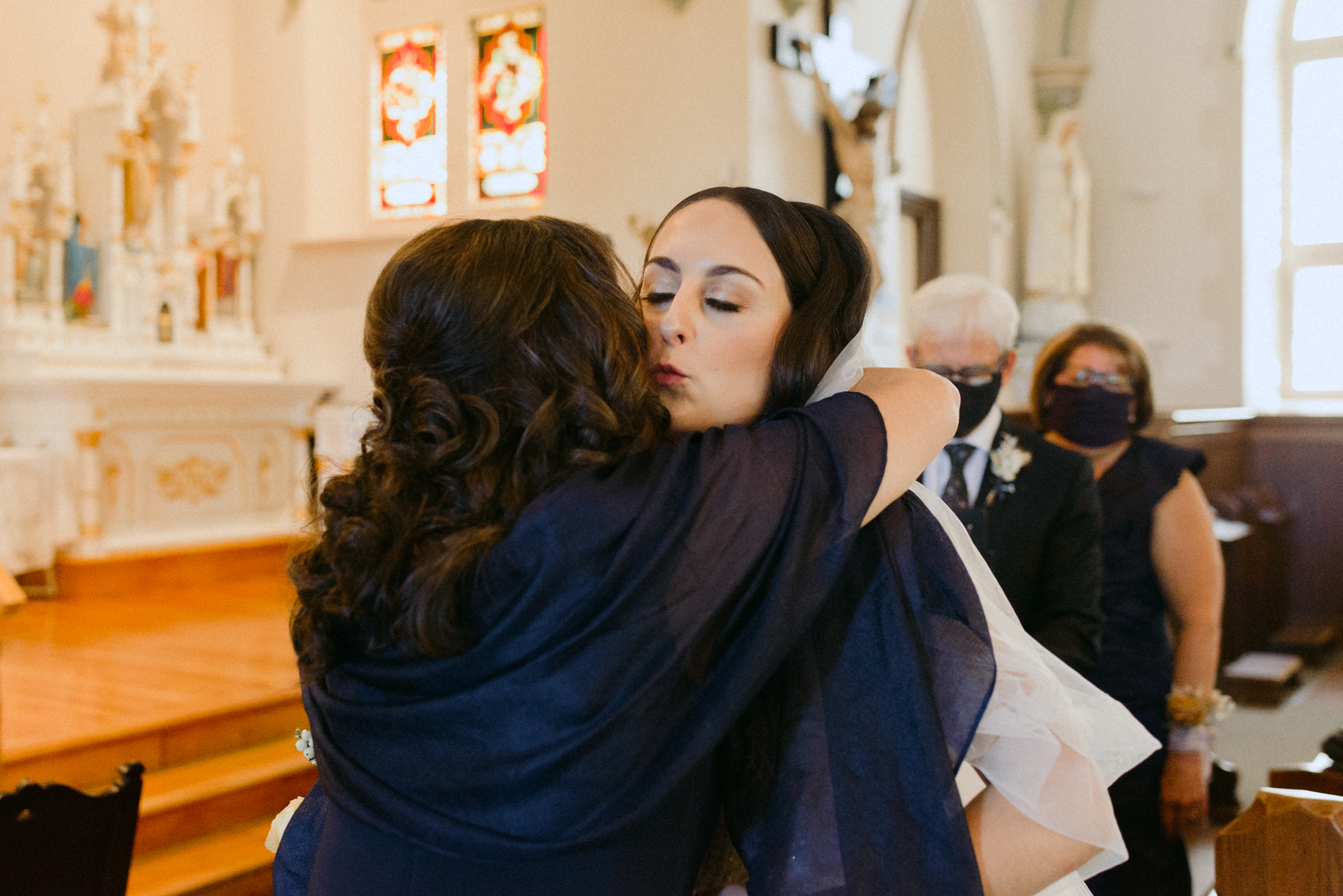 bride kissing her mother at the end of the aisle during church wedding ceremony