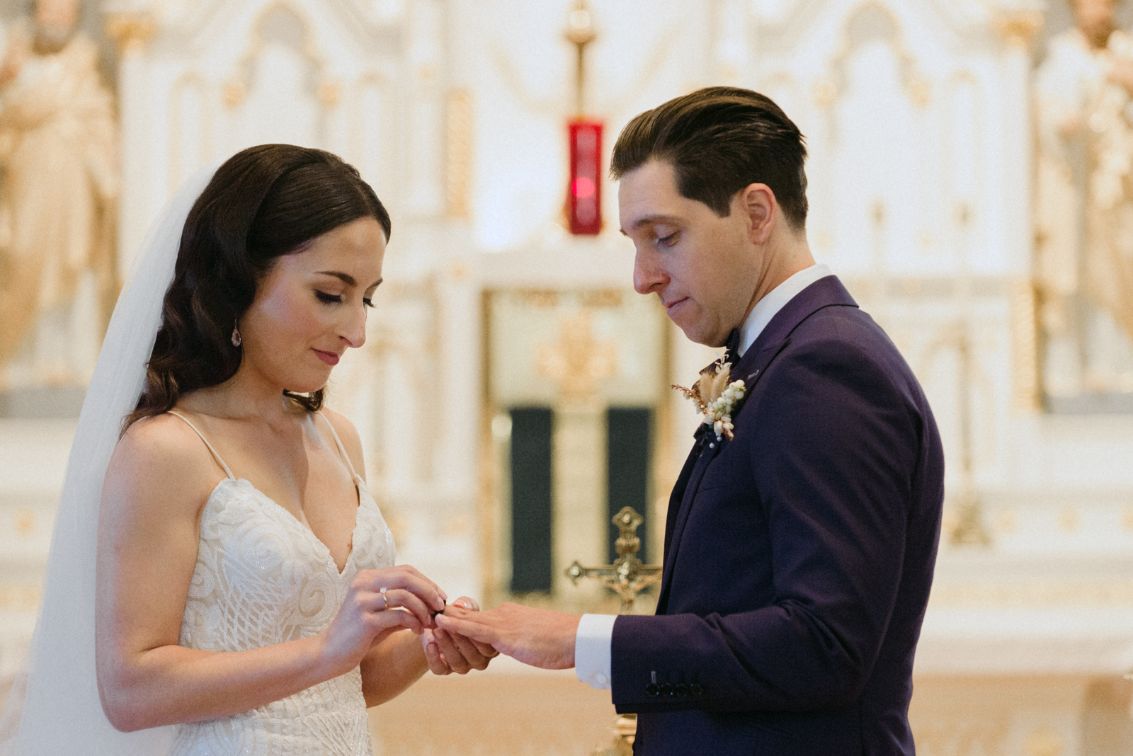 bride putting on the groom's wedding band during church wedding ceremony