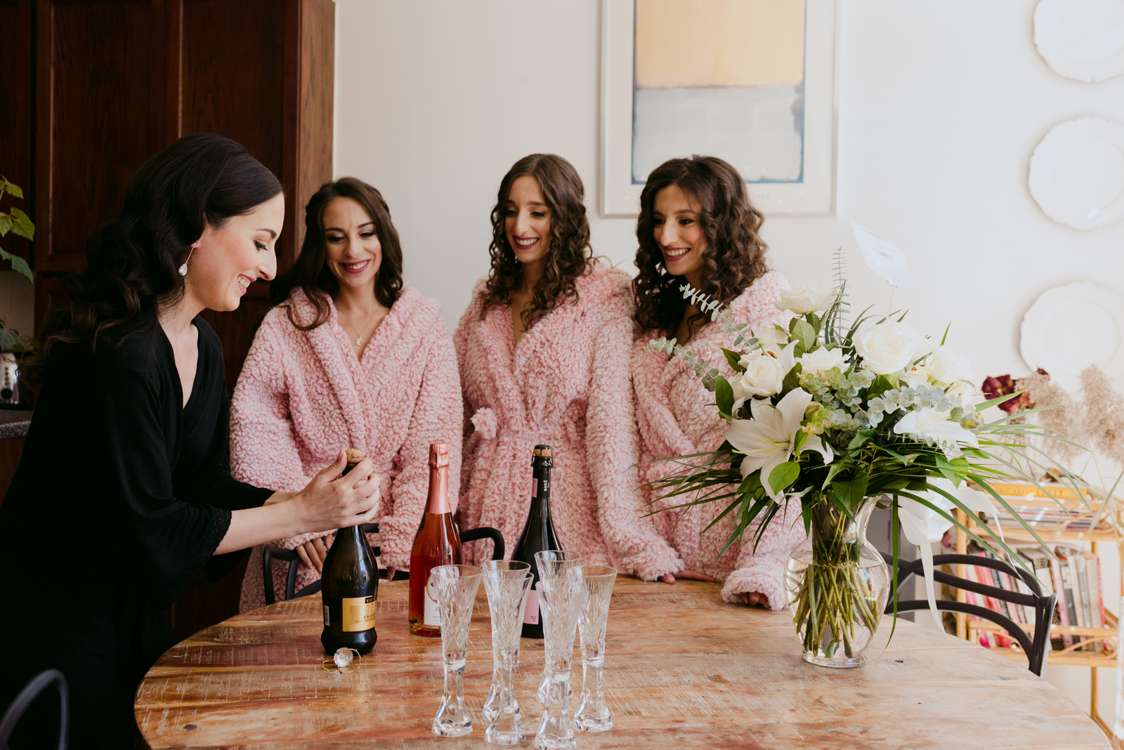 bride opening a bottle of champagne with her bridesmaids watching
