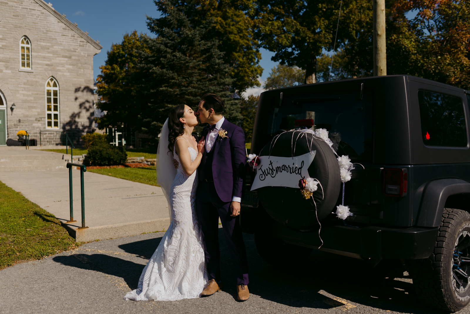 bride and groom kissing next to jeep wrangler with "just married" sign on it
