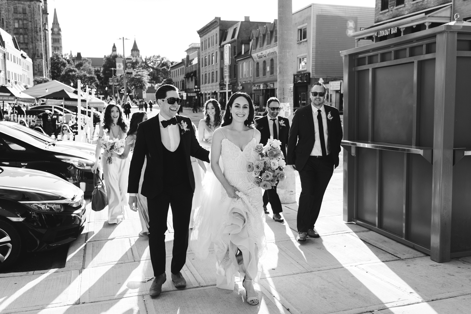 bride and groom walking with their wedding party through the byward market in black and white
