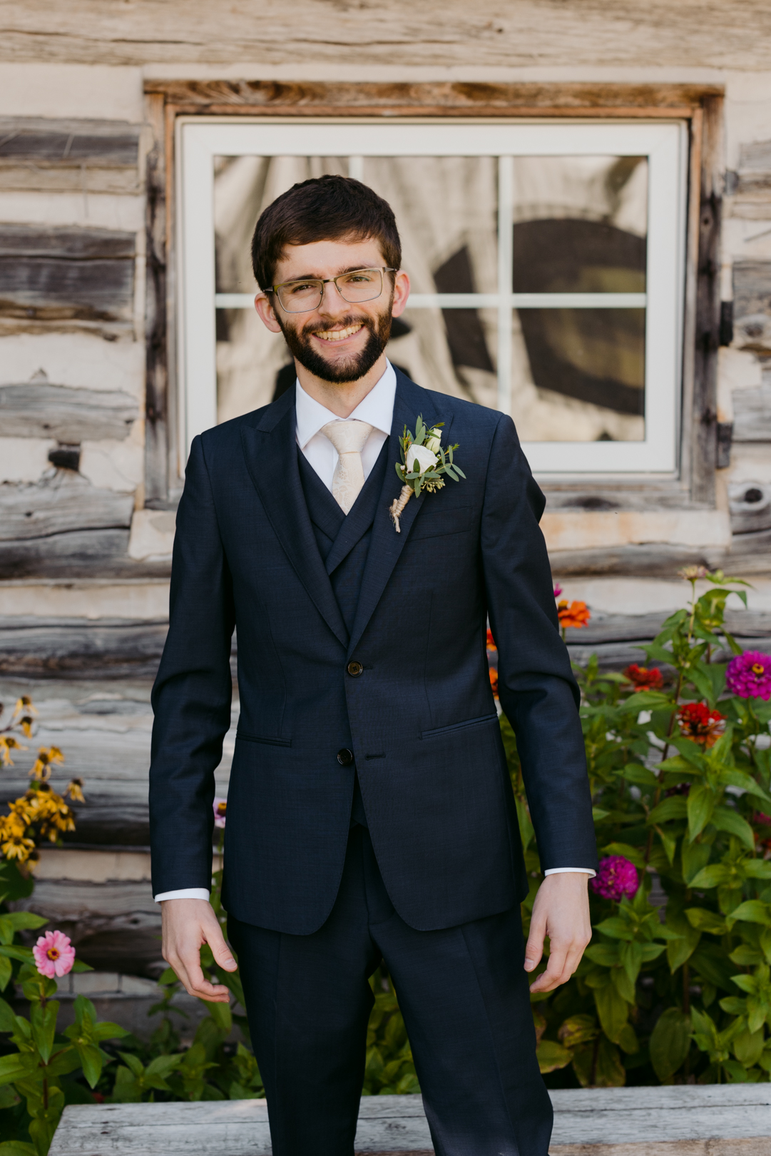 groom smiling in front of log cabin
