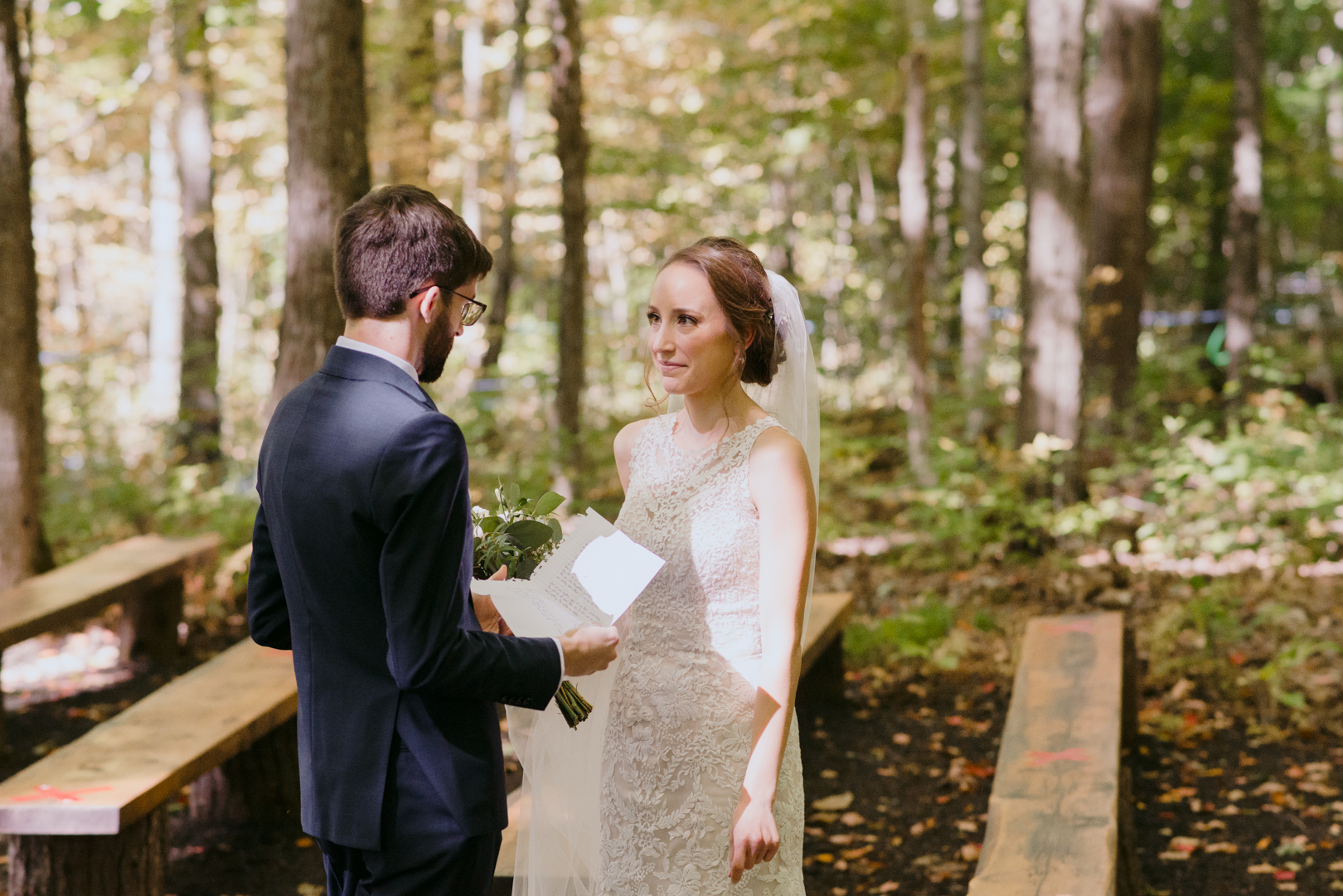bride listening to the groom as he reads her a letter in a forest after first look