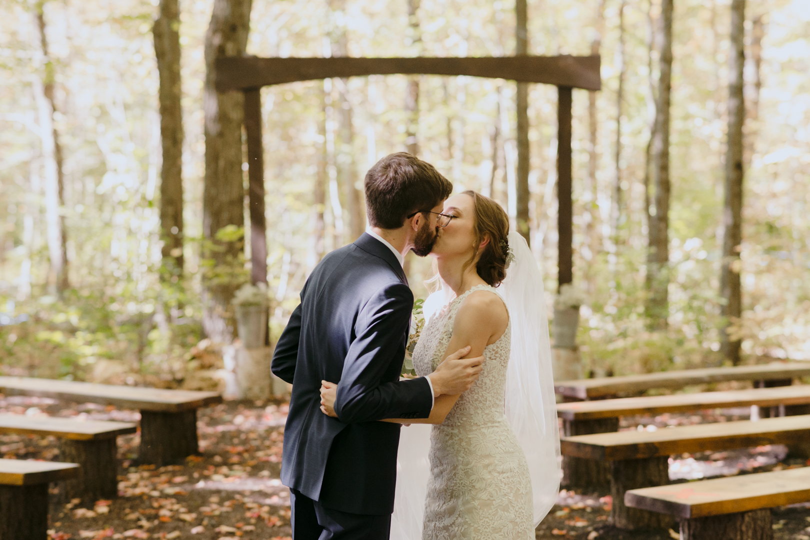 bride and groom kissing in a forest after first look