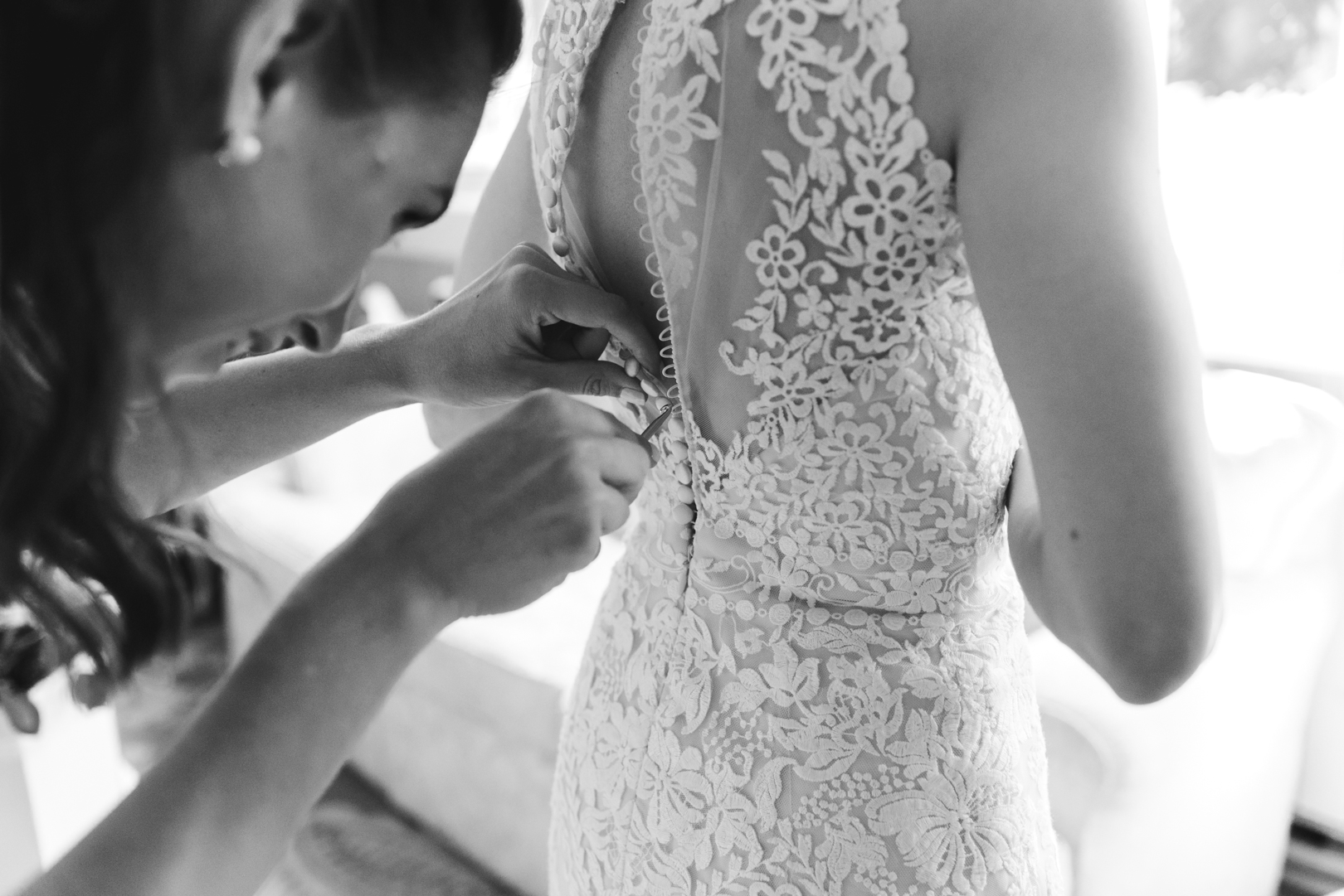 bridesmaid tying up the bride's dress with a crochet hook