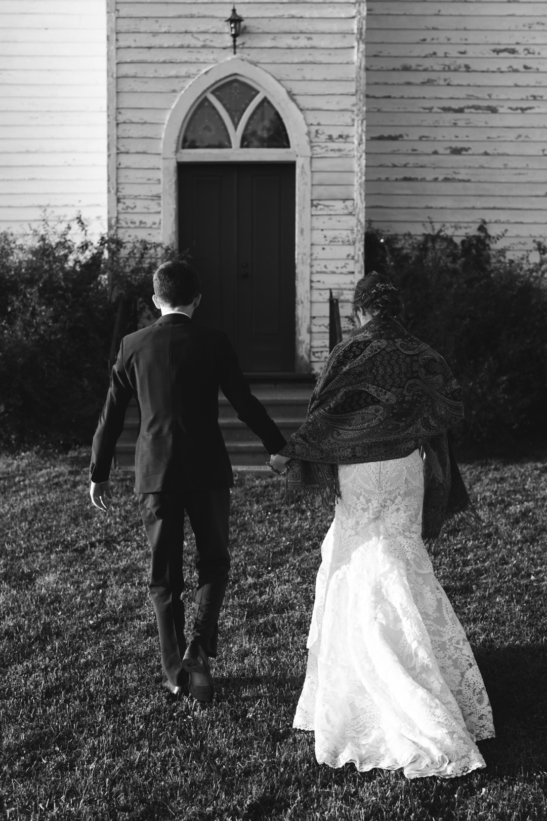 bride and groom walking towards church door in black and white