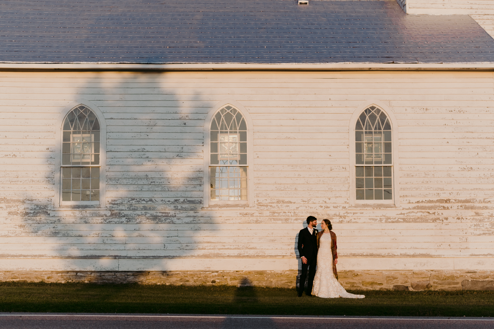 bride and groom in front of old white church at sunset