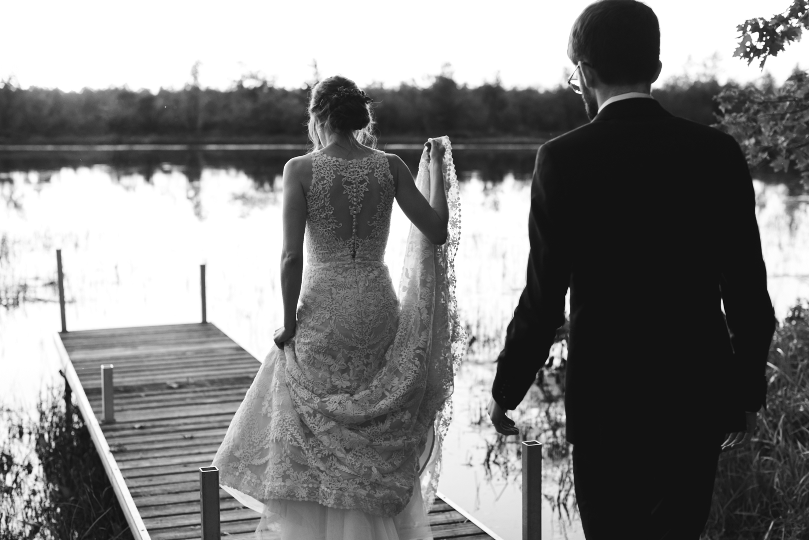 bride and groom walking out onto boat dock in black and white