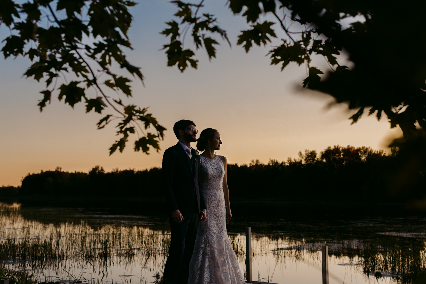 bride and groom standing by the water at sunset