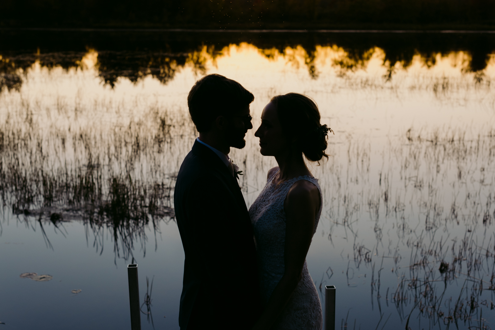 silhouette of bride and groom by the water at sunset