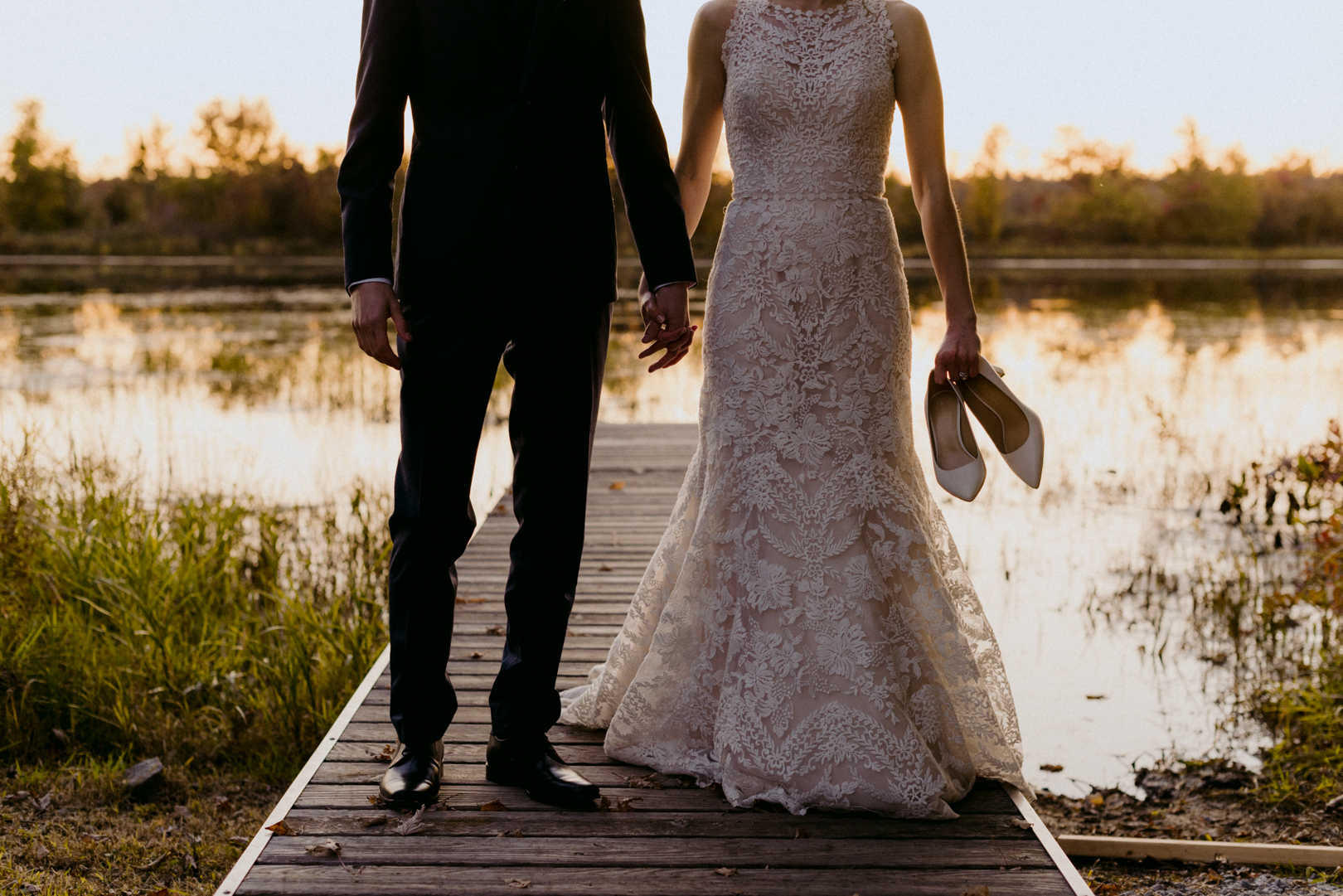 bride and groom on boat launch dock at sunset with bride holding her shoes in her hands