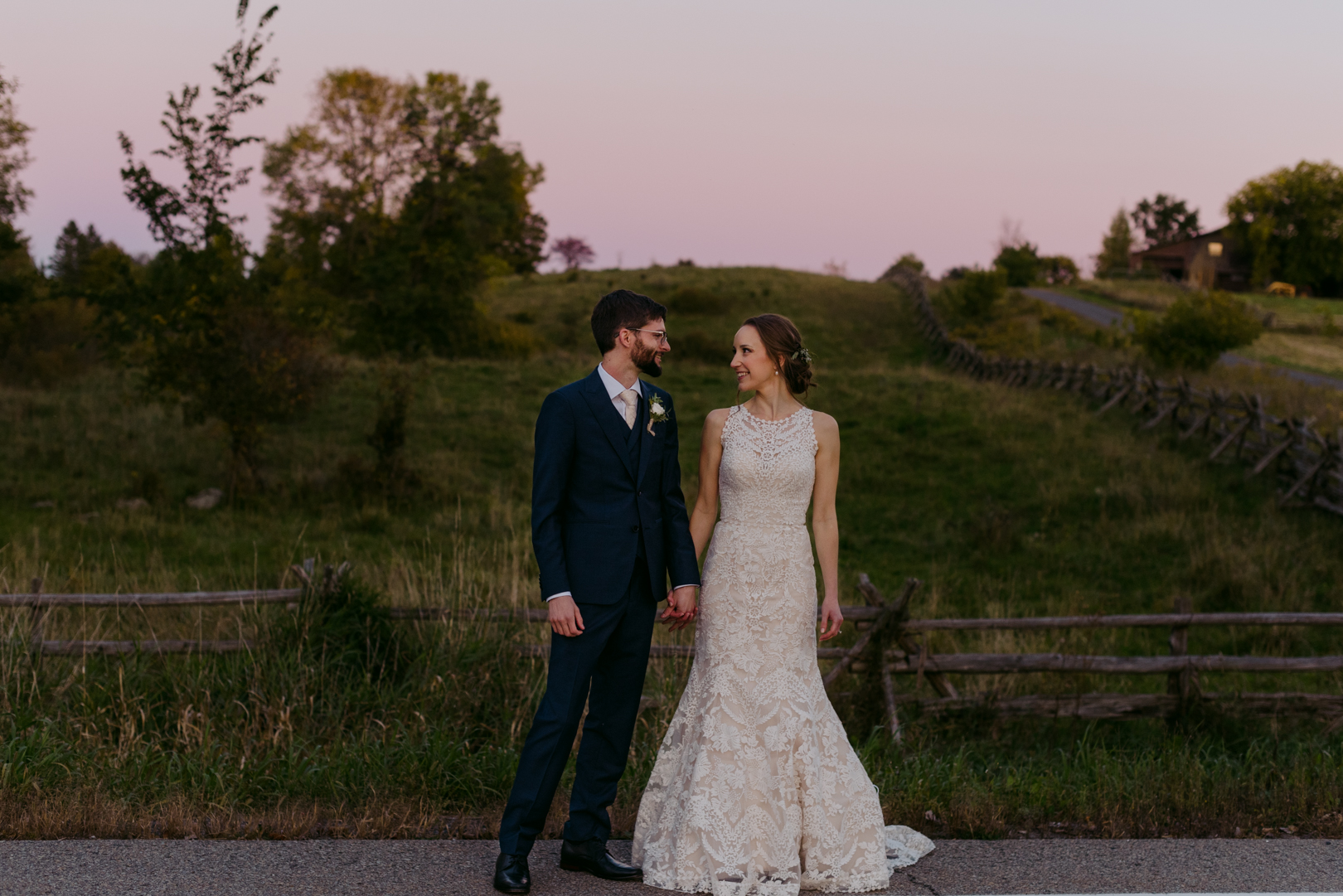 bride and groom holding hands by farmers field at sunset