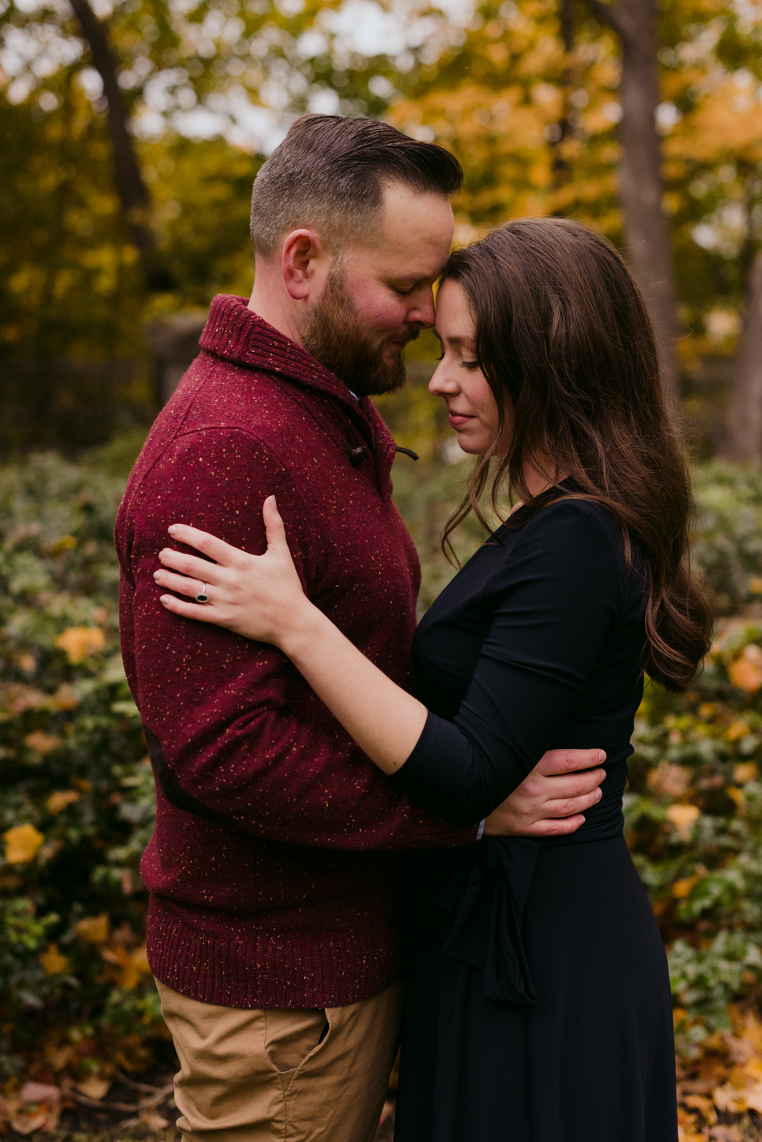 engaged couple cuddling in the leaves on a fall day