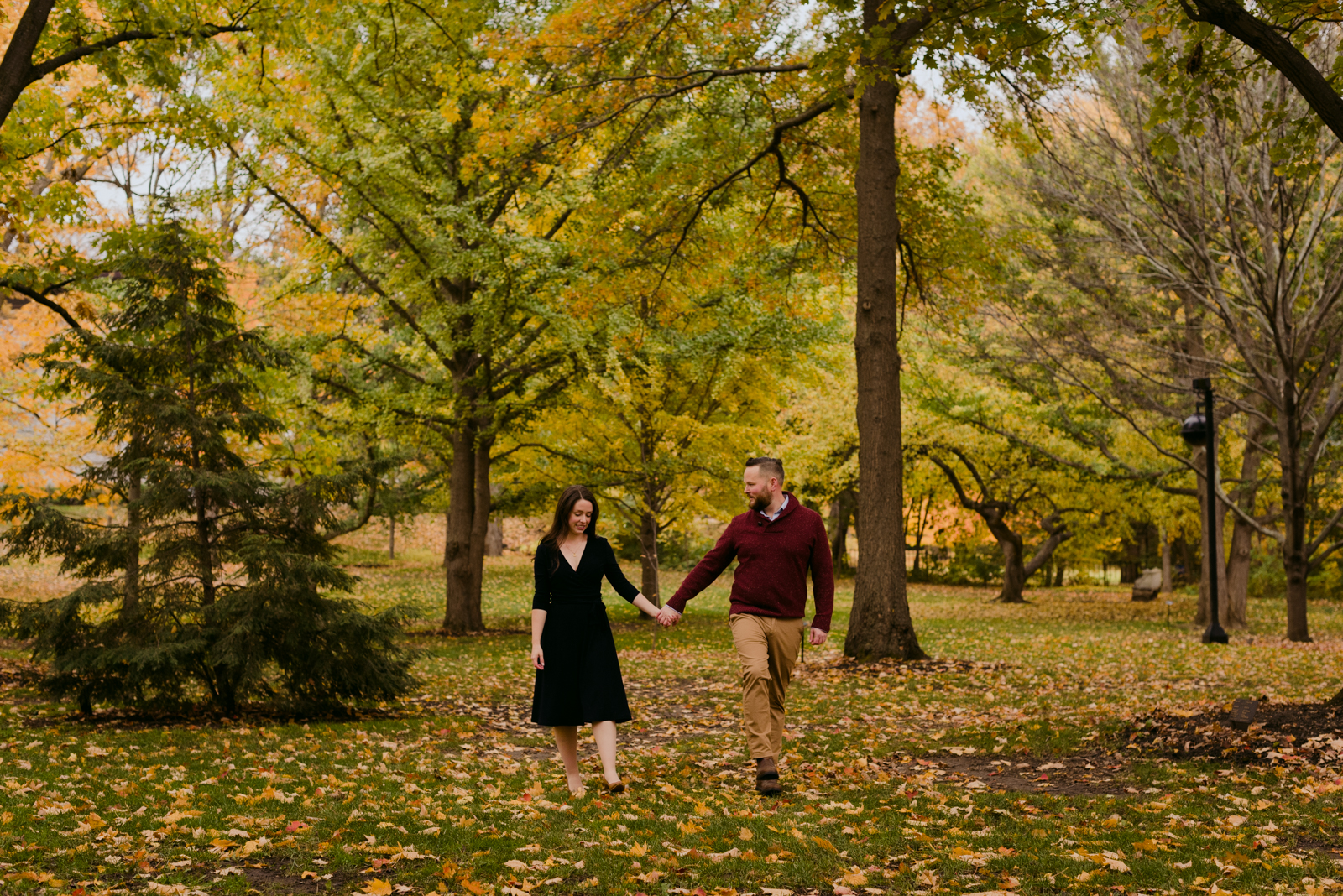 engaged couple holding hands walking through the leaves