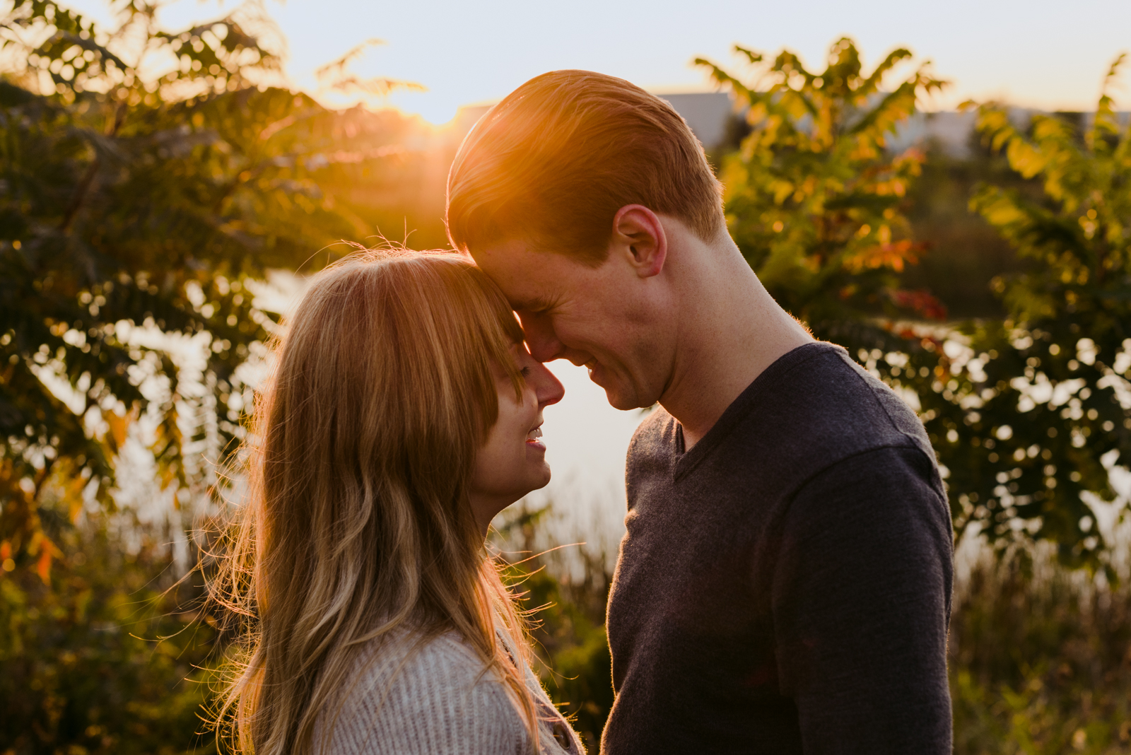 engaged couple with foreheads touching at sunset by the water