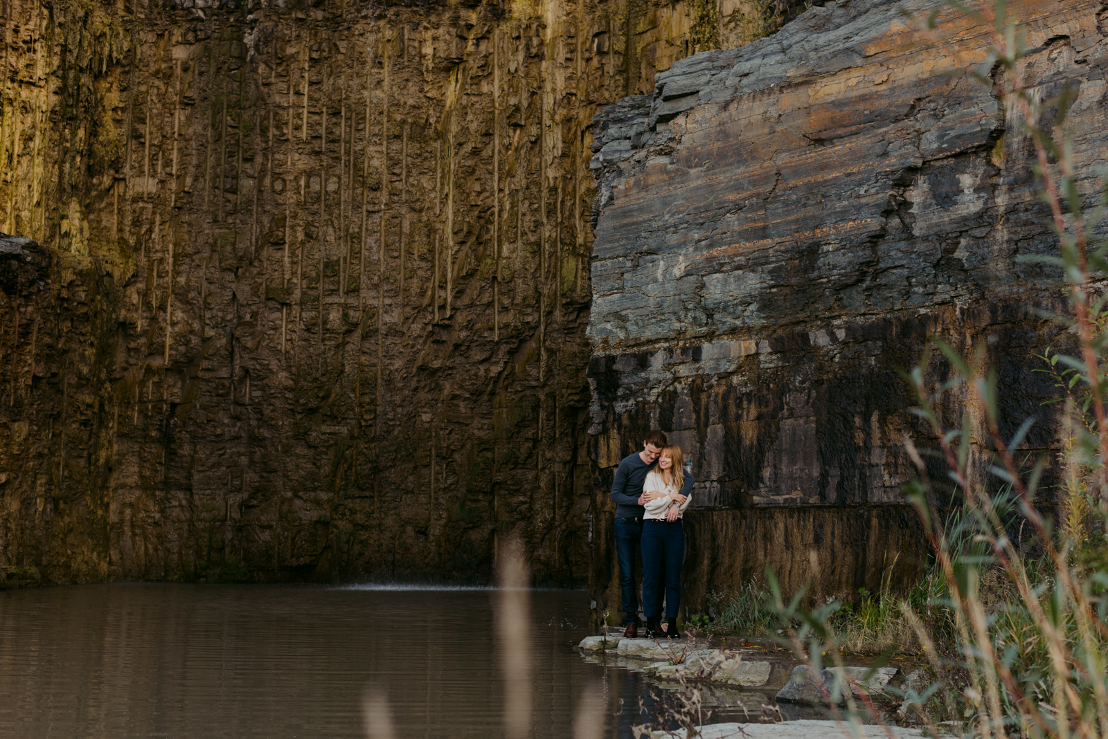 engaged couple with arms around each other standing on a rock by the quarry