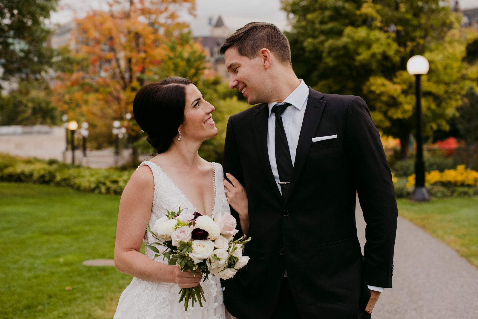 bride and groom smiling at each other on path with fall coloured trees