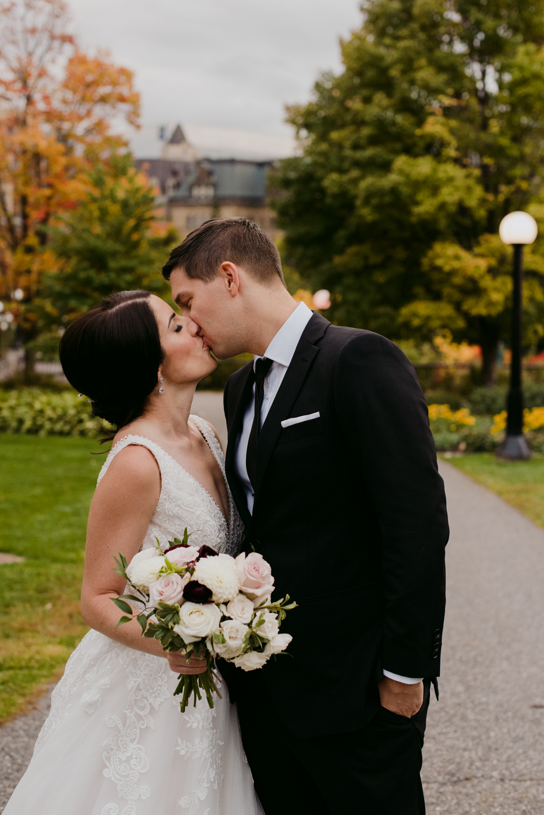 bride and groom kissing on a path with fall trees at sunset