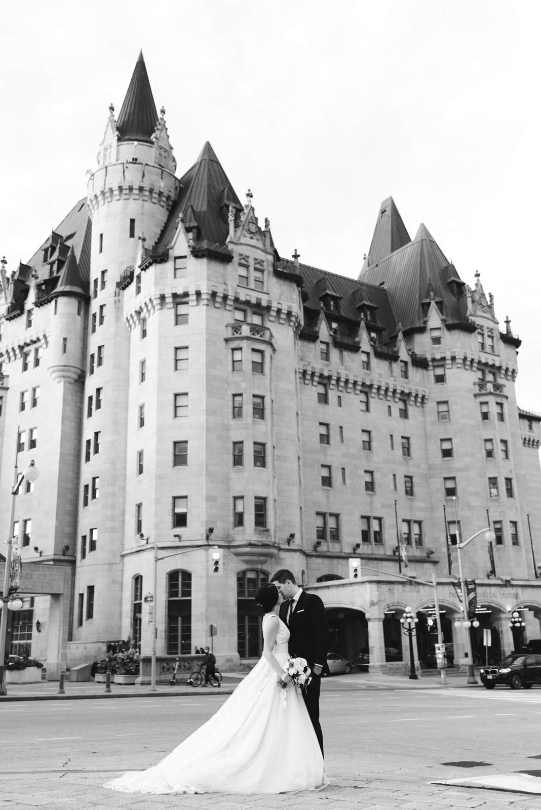 bride and groom kissing in front of chateau laurier in black and white