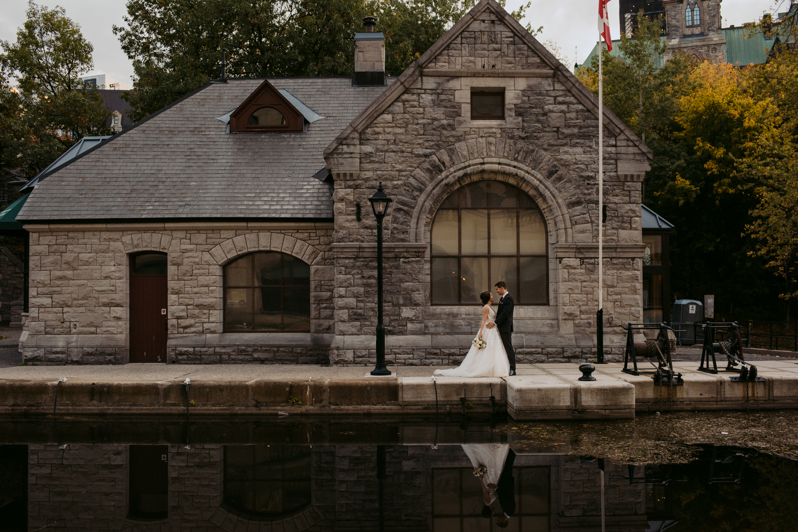 bride and groom in front of old stone building by the canal in ottawa