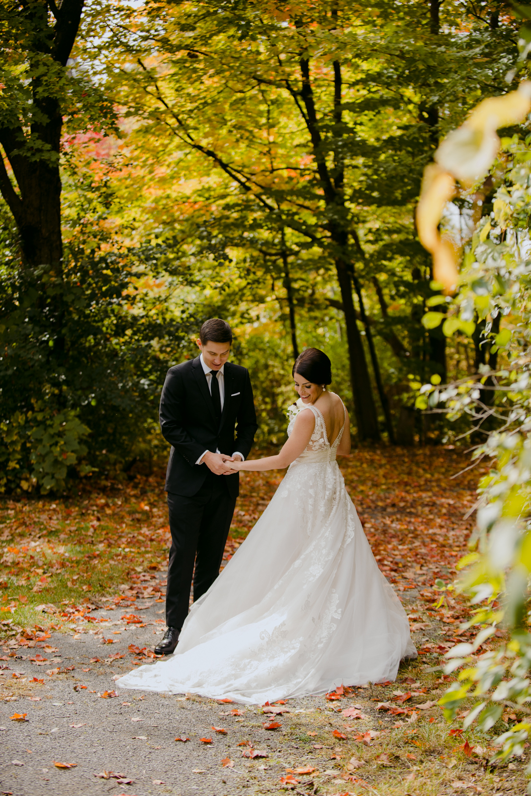 groom checking out the bride's dress on path with fall coloured leaves
