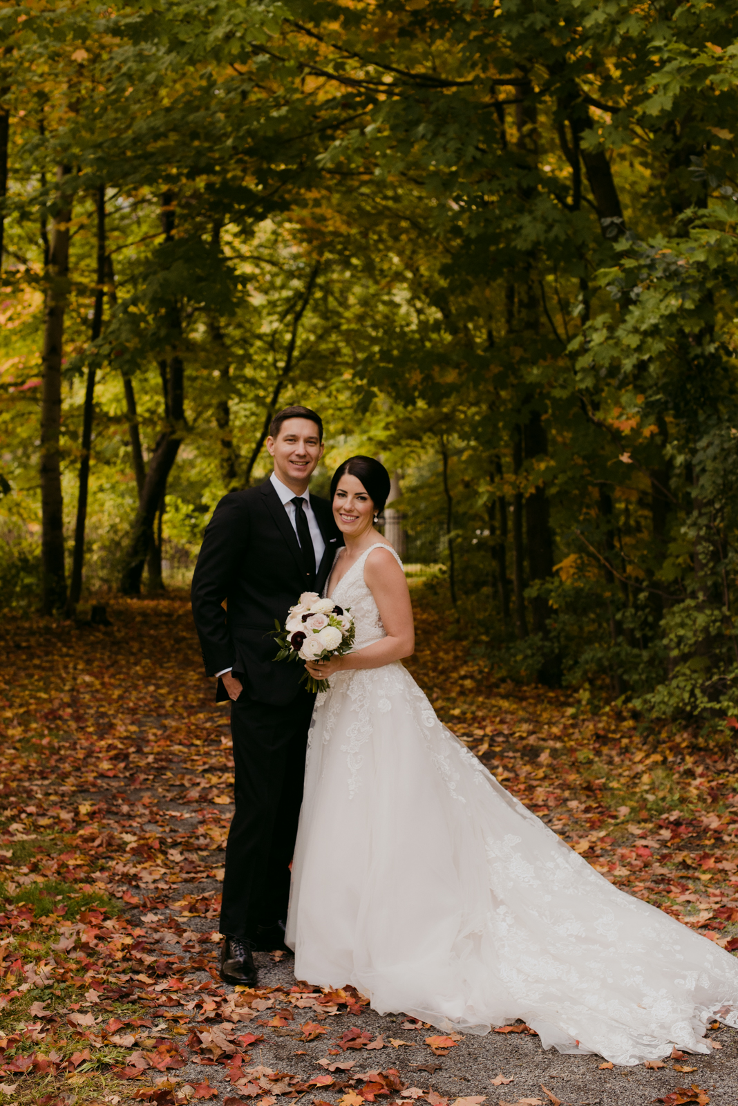 bride and groom smiling on fall path with leaves on the ground