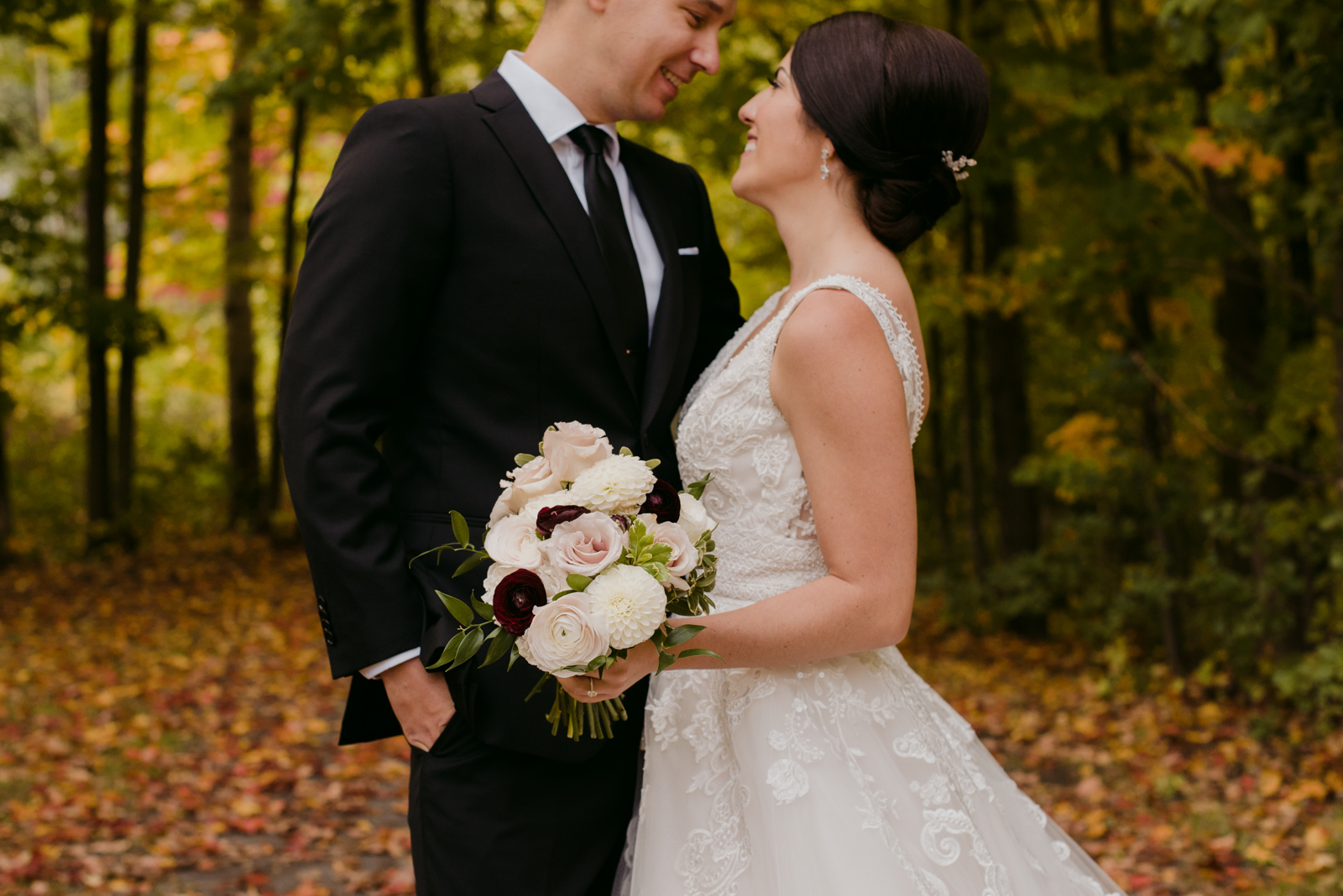bride and groom cuddling close on path with fall leaves all around