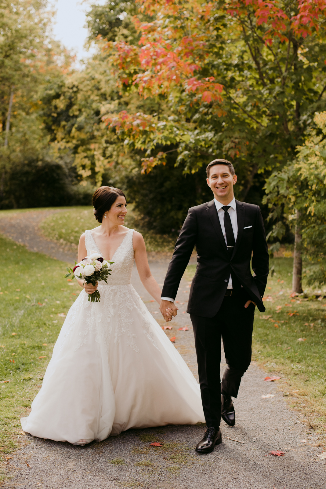 bride and groom holding hands walking down path with fall leaves