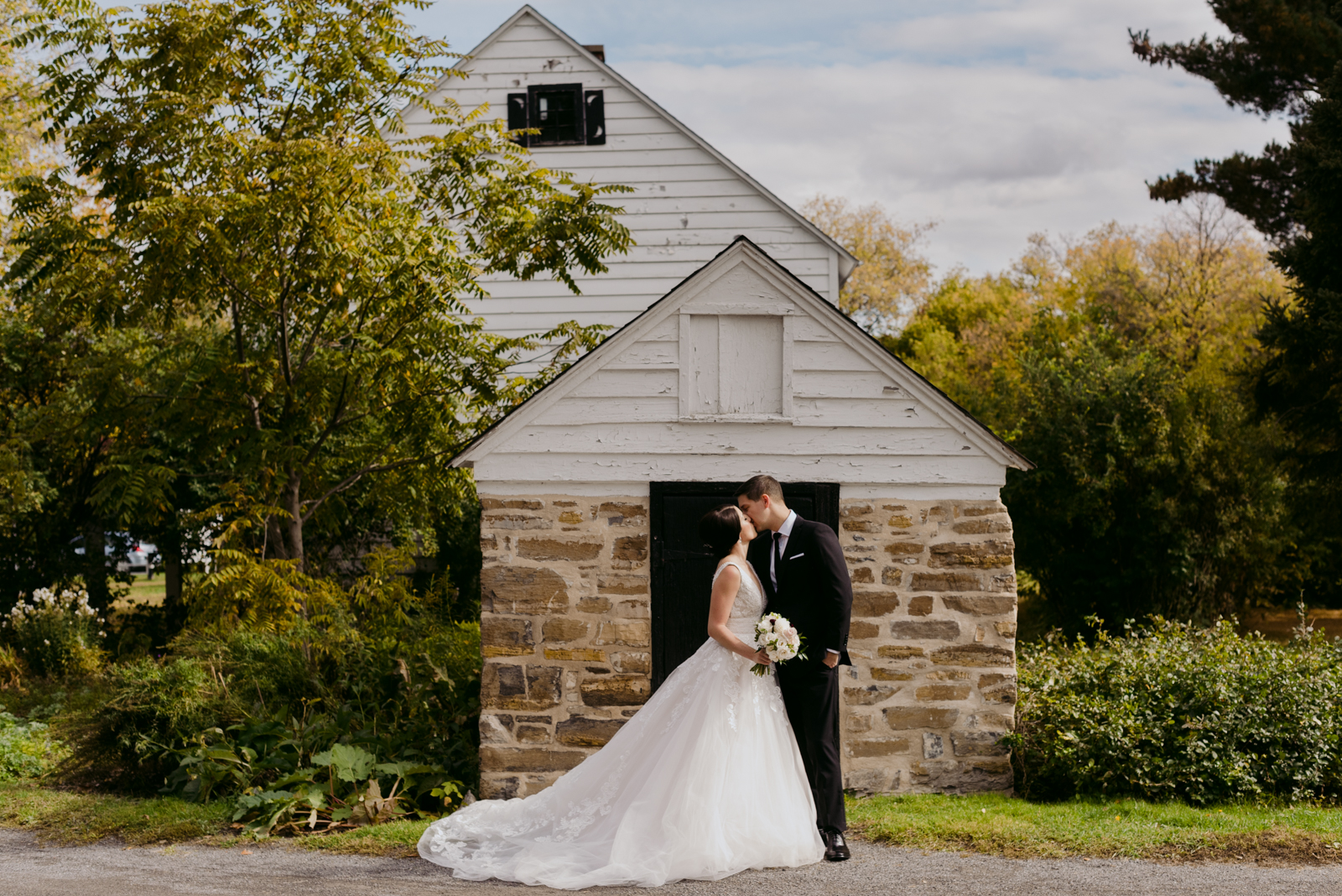 bride and groom kissing in front of stone smoke house at the billings estate museum