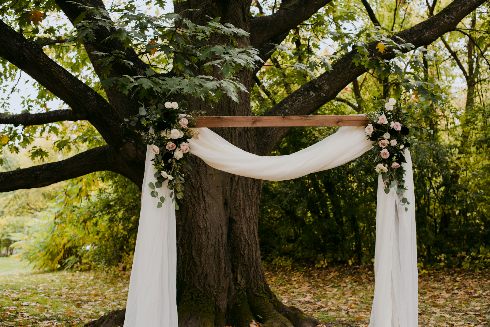 wooden wedding arch with flowers and drapery at outdoor wedding ceremony